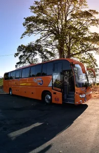 TRACOPA bus in Costa Rica, commonly used for traveling to explore things to do in Uvita, parked under a large tree on a sunny day.