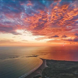 A breathtaking sunset over Marino Ballena National Park in Uvita, Costa Rica, showcasing the famous Whale Tail sandbar formation as the sky radiates with vibrant hues of orange, pink, and purple. This serene natural wonder is one of the top things to do in Uvita, offering visitors the perfect setting for beach walks, wildlife observation, and sunset views.