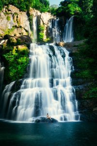 A mesmerizing view of Nauyaca Waterfalls in Costa Rica, with cascading tiers of water flowing into a pristine pool below. A lone woman sits on a rock at the base of the waterfall, enjoying the serene beauty and refreshing mist. This natural gem, surrounded by lush green foliage, is one of the top things to do in Uvita, offering visitors a chance to connect with nature and experience the tranquility of Costa Rica’s wilderness.