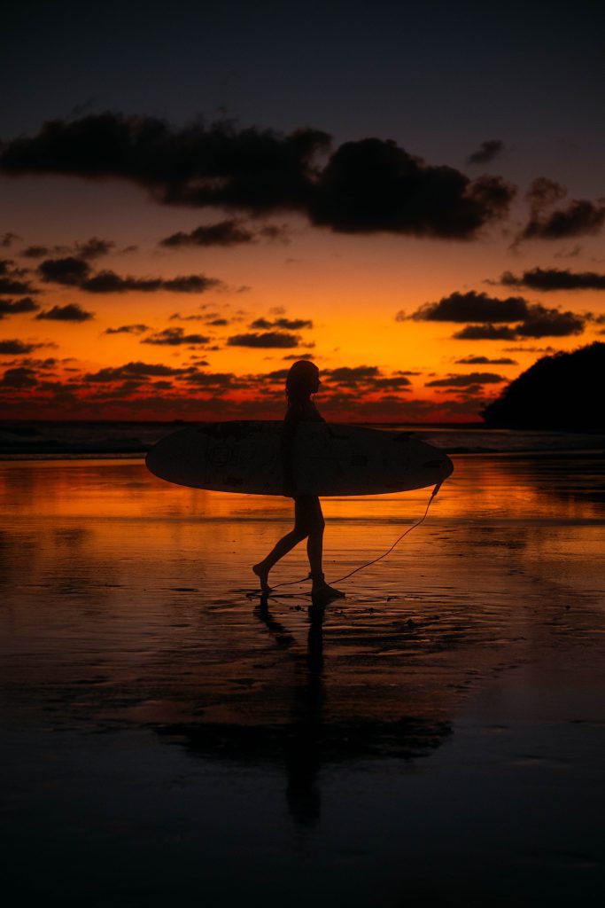 woman carrying surf board at sunset while staying a boutique hotel in Uvita Costa Rica 