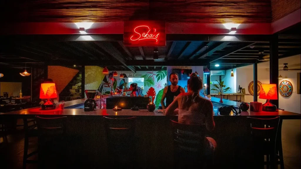 Nighttime view of the bar at Sebas Restaurant in Uvita, Costa Rica, one of the best restaurants in Uvita, with a neon sign and patrons at the bar. It is a short drive from Vayu Retreat Villas 