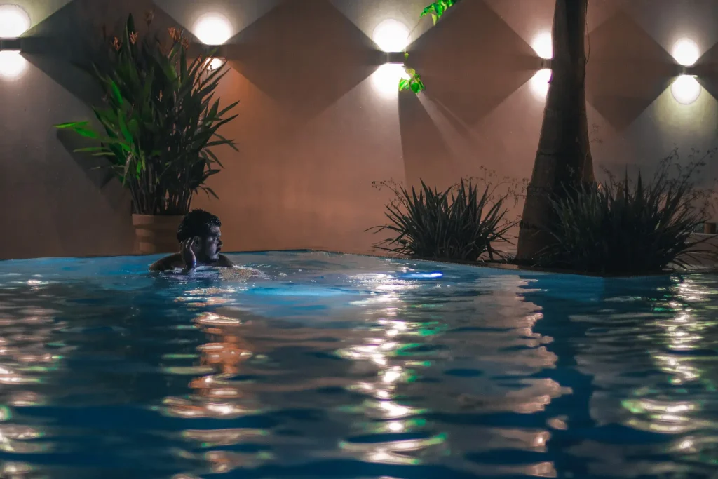 A man enjoys a nighttime swim in the illuminated pool at Vayu Retreat Villas, surrounded by lush plants and ambient lighting. This serene scene highlights the luxurious ambiance of one of the best hotels in Uvita, Costa Rica, perfect for a relaxing jungle retreat.