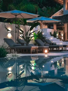 A serene night view of the pool area at boutique hotel in costa rica Vayu Retreat Villas, with illuminated lounge chairs and umbrellas reflected in the water. This inviting scene captures the luxurious ambiance of one of the best hotels in Uvita, Costa Rica, perfect for a tranquil and elegant jungle retreat experience.