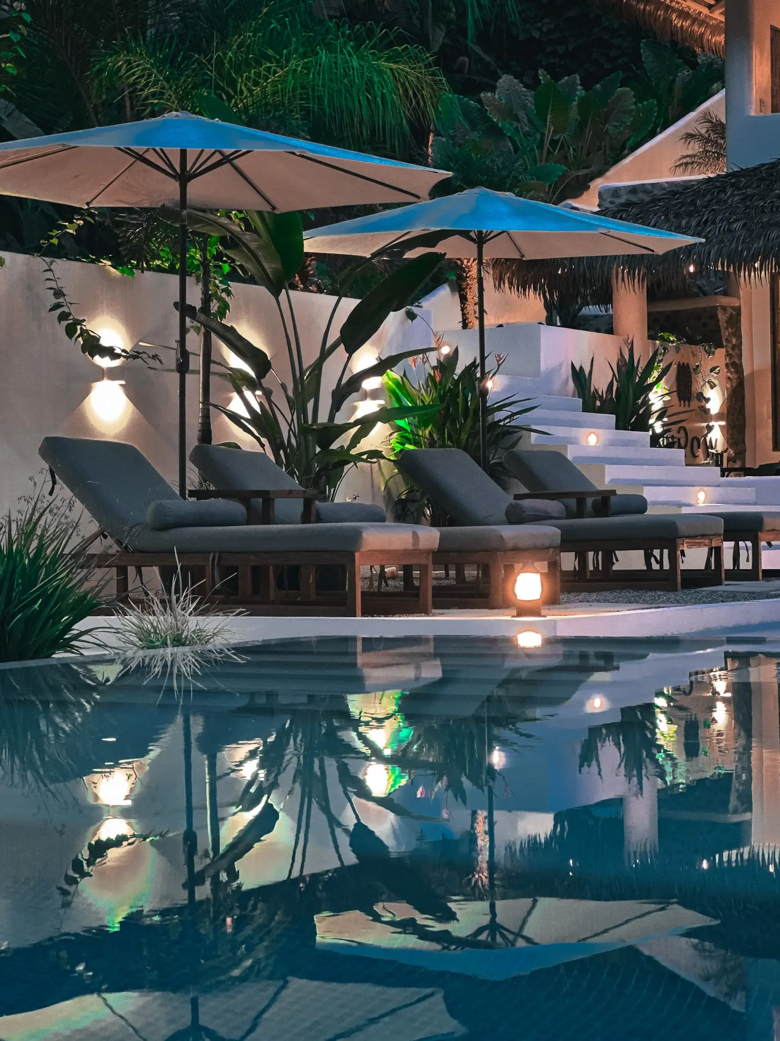 A serene night view of the pool area at Vayu Retreat Villas, with illuminated lounge chairs and umbrellas reflected in the water. This inviting scene captures the luxurious ambiance of one of the best hotels in Uvita, Costa Rica, perfect for a tranquil and elegant jungle retreat experience.