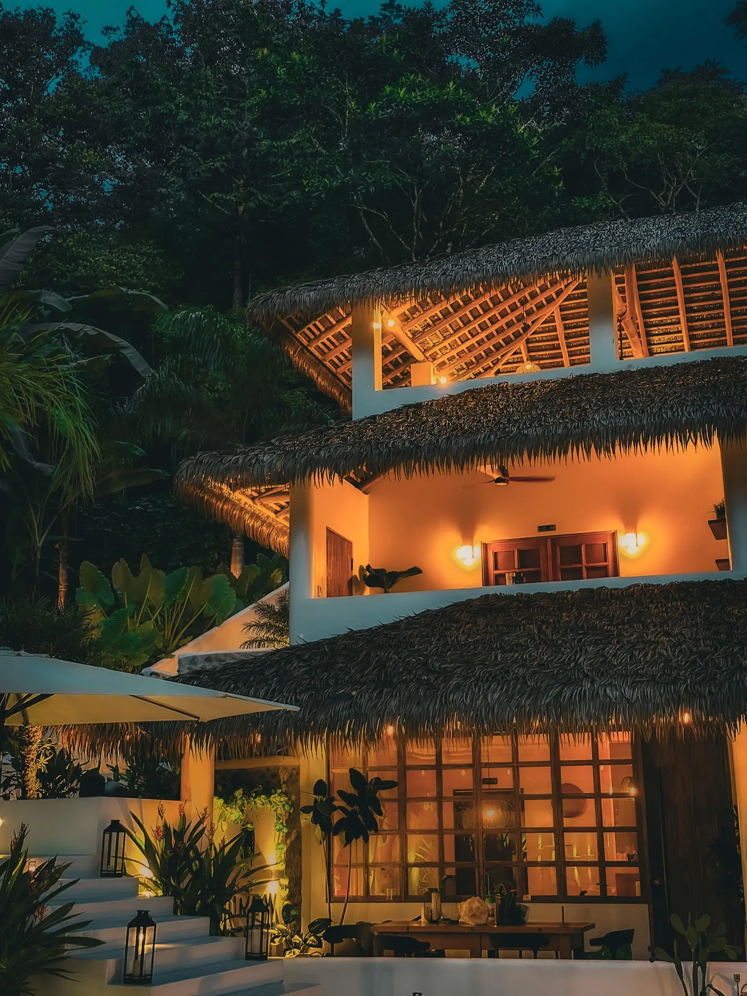 A stunning view of Vayu Retreat Villas at dusk, showcasing the beautifully illuminated thatched-roof structure surrounded by lush jungle greenery. This enchanting image highlights one of the best hotels in Uvita, Costa Rica, perfect for those seeking a serene and luxurious jungle retreat.