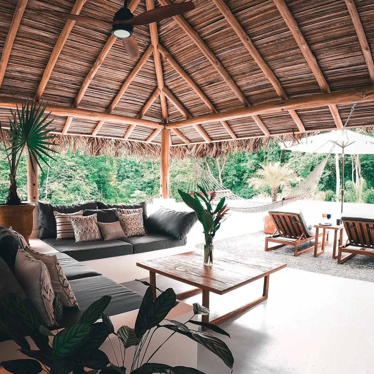 An inviting outdoor lounge area at Vayu Retreat Villas, featuring a cozy sofa set under a thatched roof gazebo with views of the lush jungle. The scene includes comfortable seating, a hammock, and a wooden coffee table, capturing the essence of one of the best hotels in Uvita, Costa Rica, known for its serene and luxurious jungle retreat atmosphere.