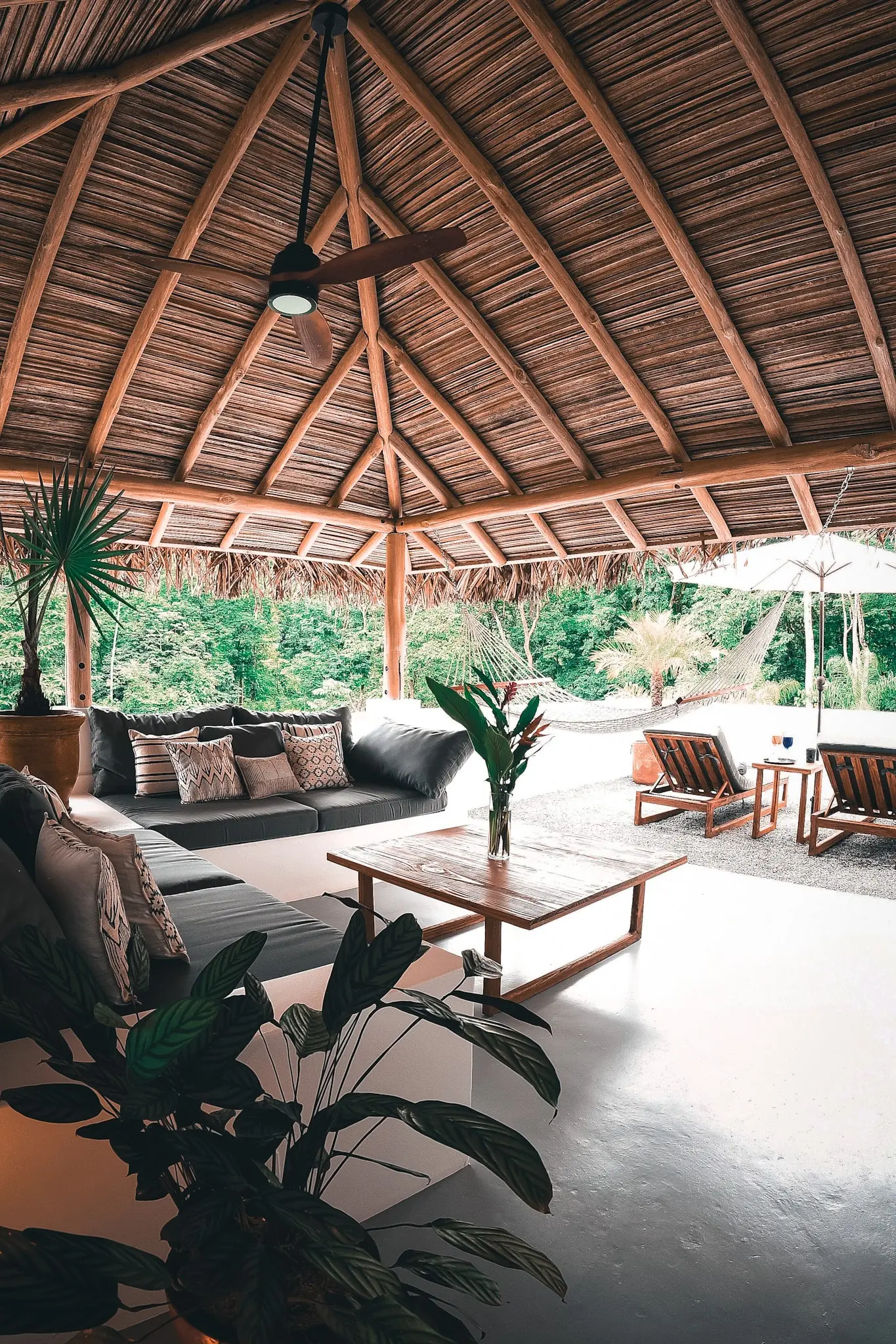 An inviting outdoor lounge area at Vayu Retreat Villas, featuring a cozy sofa set under a thatched roof gazebo with views of the lush jungle. The scene includes comfortable seating, a hammock, and a wooden coffee table, capturing the essence of one of the best hotels in Uvita, Costa Rica, known for its serene and luxurious jungle retreat atmosphere.