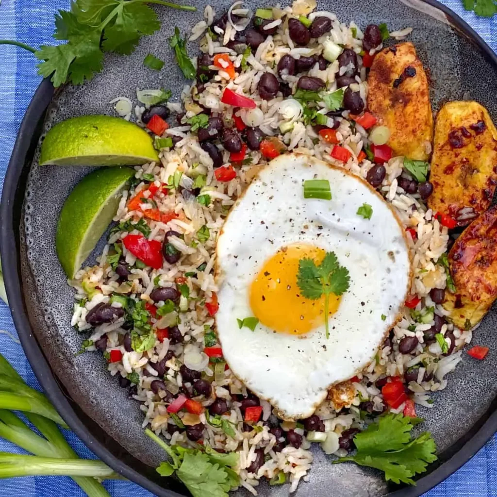 A traditional Costa Rican gallo pinto dish served at a soda restaurant Costa Rica, featuring rice and beans, a sunny-side-up egg, grilled plantains, and fresh lime wedges.