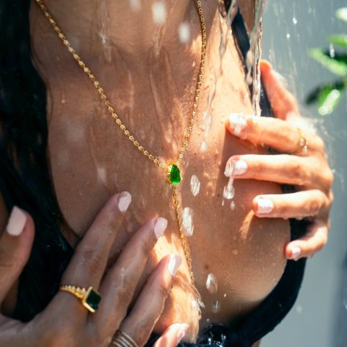 Woman Wearing Jewelry Under a Tropical Shower - A woman adorned with gold jewelry, including a green gemstone necklace, enjoys a refreshing outdoor shower. The photo captures the essence of luxury and relaxation during a vacation in Costa Rica's Green Season.