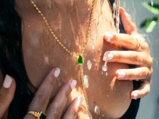 Woman Wearing Jewelry Under a Tropical Shower - A woman adorned with gold jewelry, including a green gemstone necklace, enjoys a refreshing outdoor shower. The photo captures the essence of luxury and relaxation during a vacation in Costa Rica's Green Season.