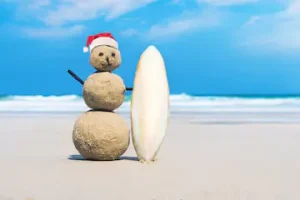 A playful sand snowman with a Santa hat and surfboard on the beach, showcasing a fun way to celebrate Christmas in Costa Rica, close to Vayu Retreat Villas